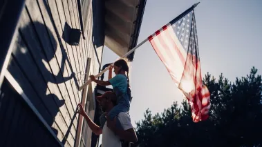 Father and daughter hang an American flag outside their home